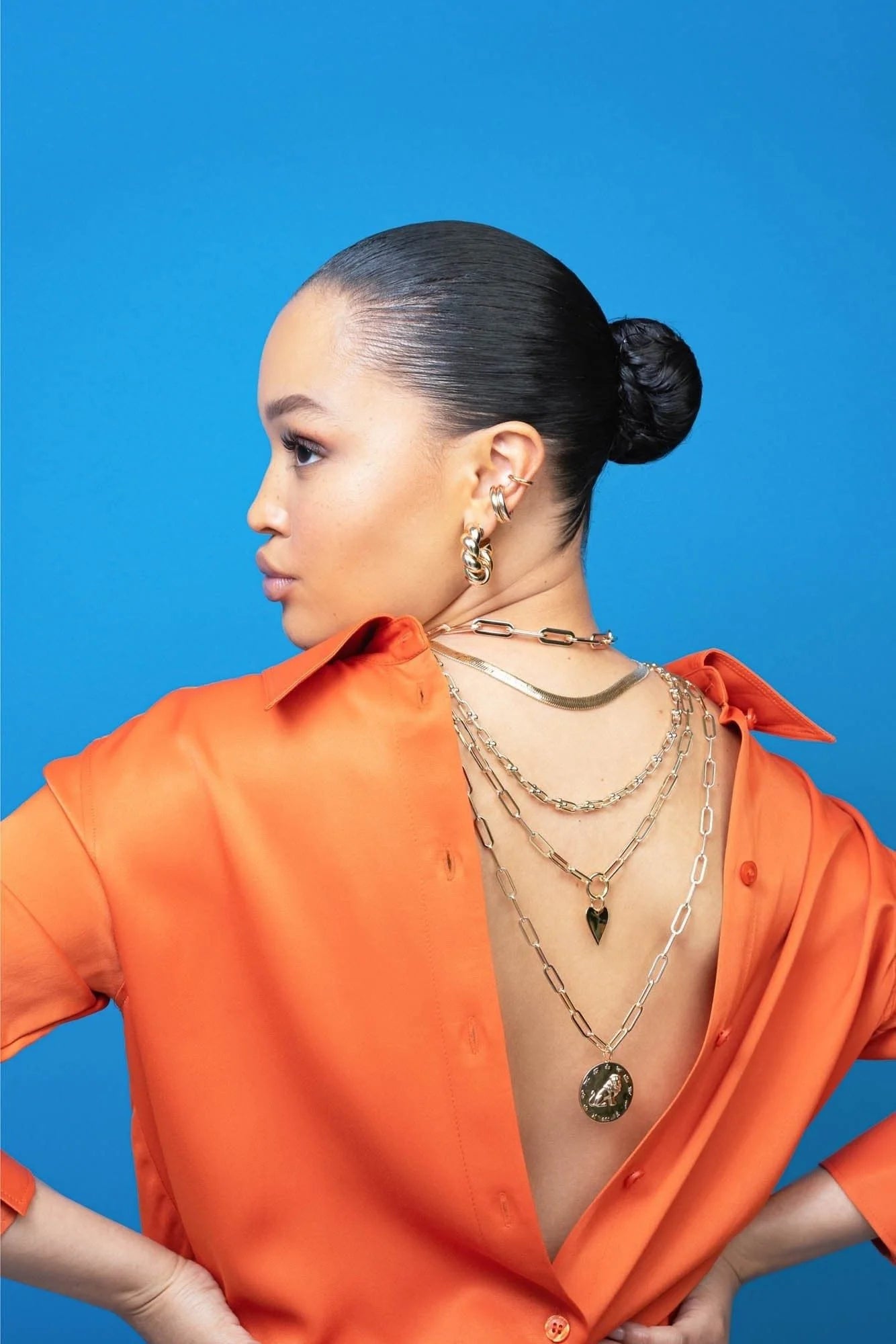 Woman wearing an orange shirt and gold necklaces with zodiac pendant Taurus Earth sign symbolized