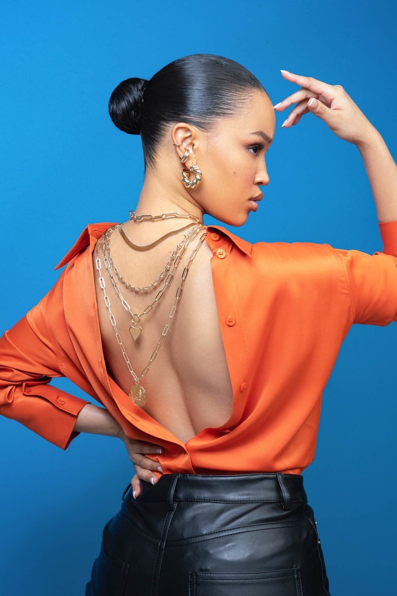 Woman in orange shirt showcasing layered gold necklaces and a Zodiac Pendant Virgo